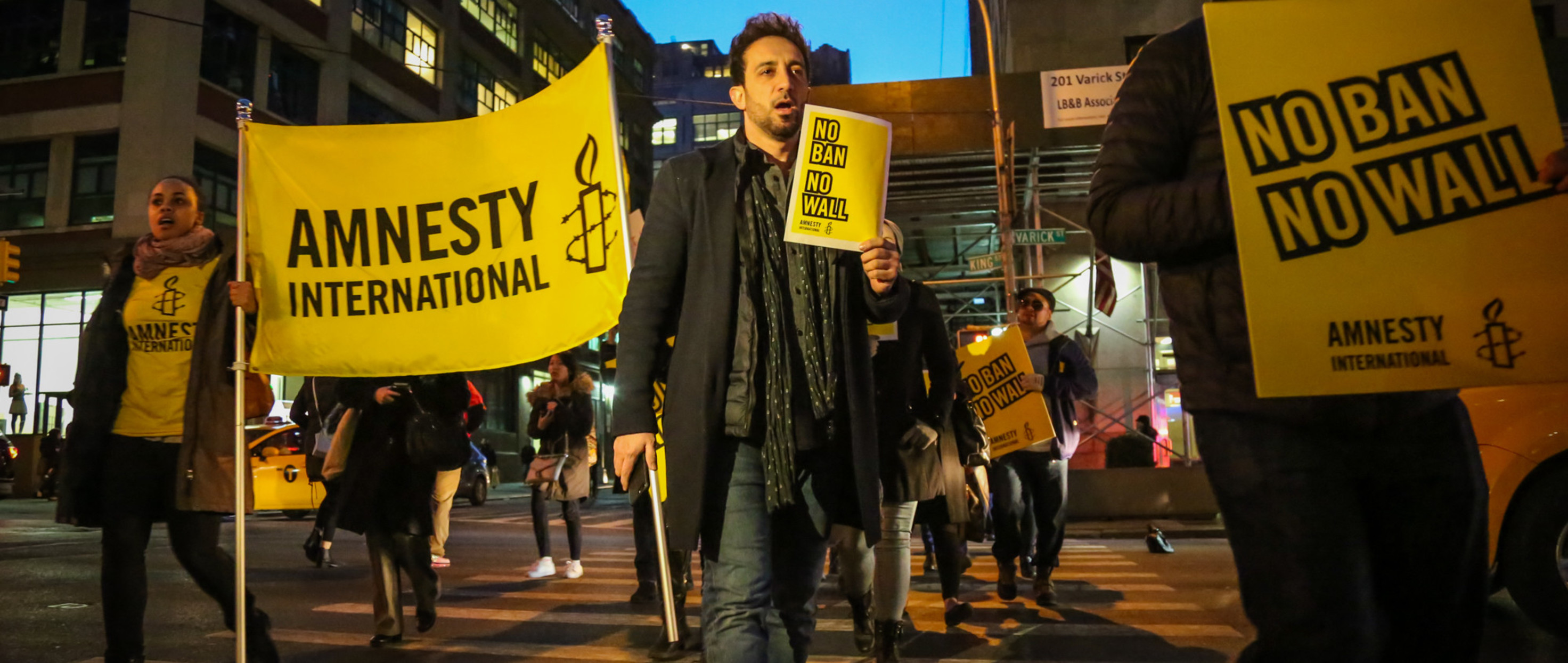 People at a protest holding Amnesty signs and signs that read "No Ban No Wall"