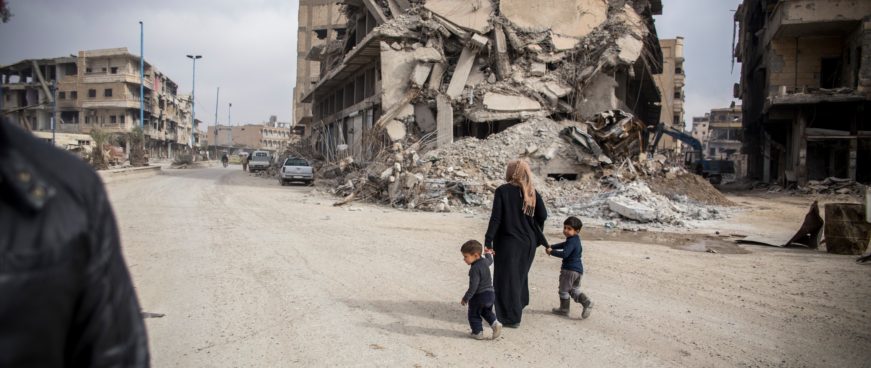 A women and her 2 children walk through the rubble in Syria