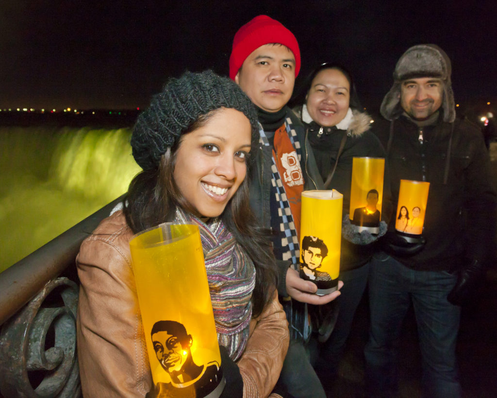 A group of people holding candles covered in Amnesty wraps with people from campaigns on them