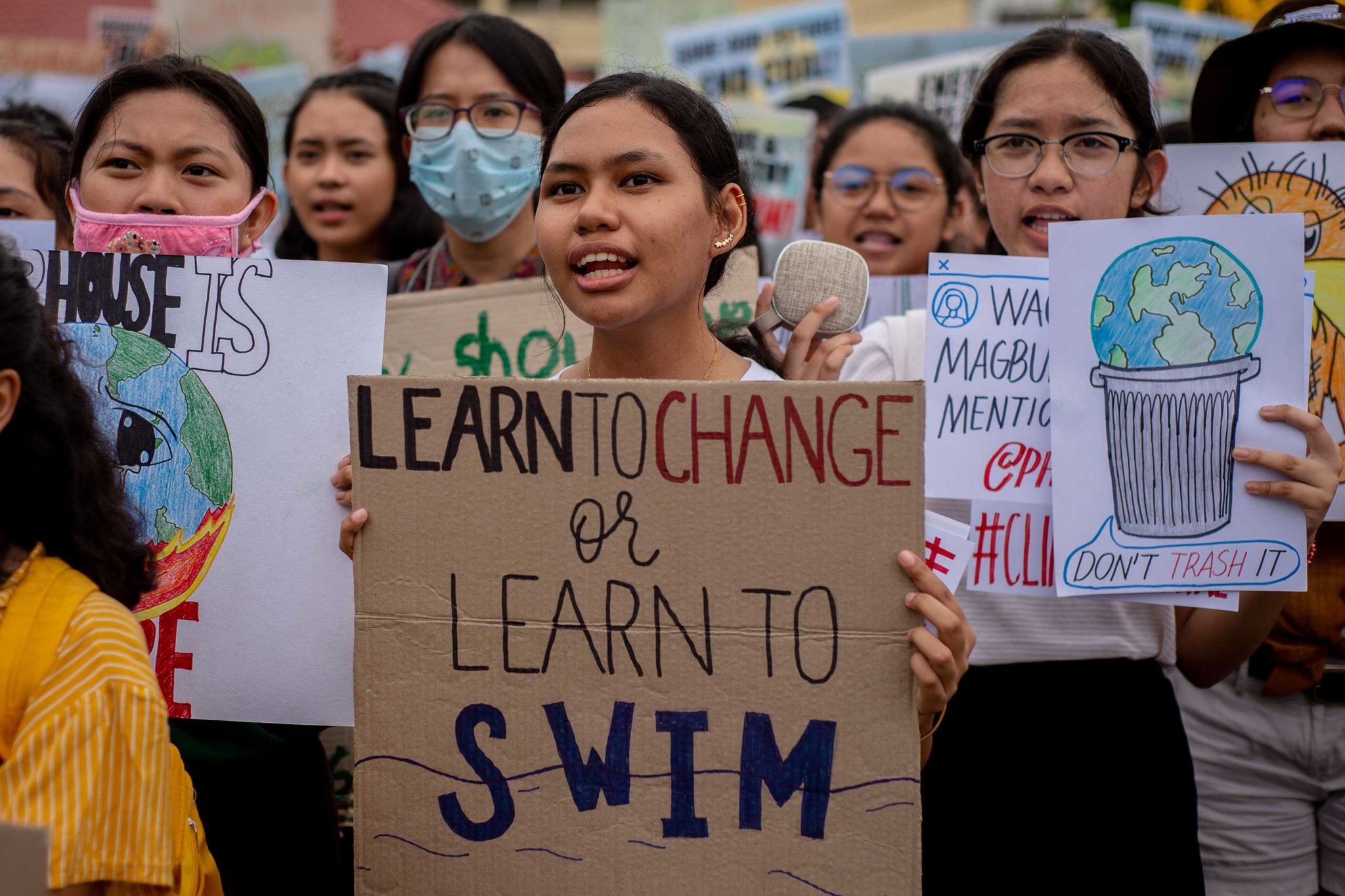 A young Filipino girl with dark hair pulled back into a ponytail holds a sign that reads 'Learn to change of learn to swim' at the September 2019 Climate Strike.