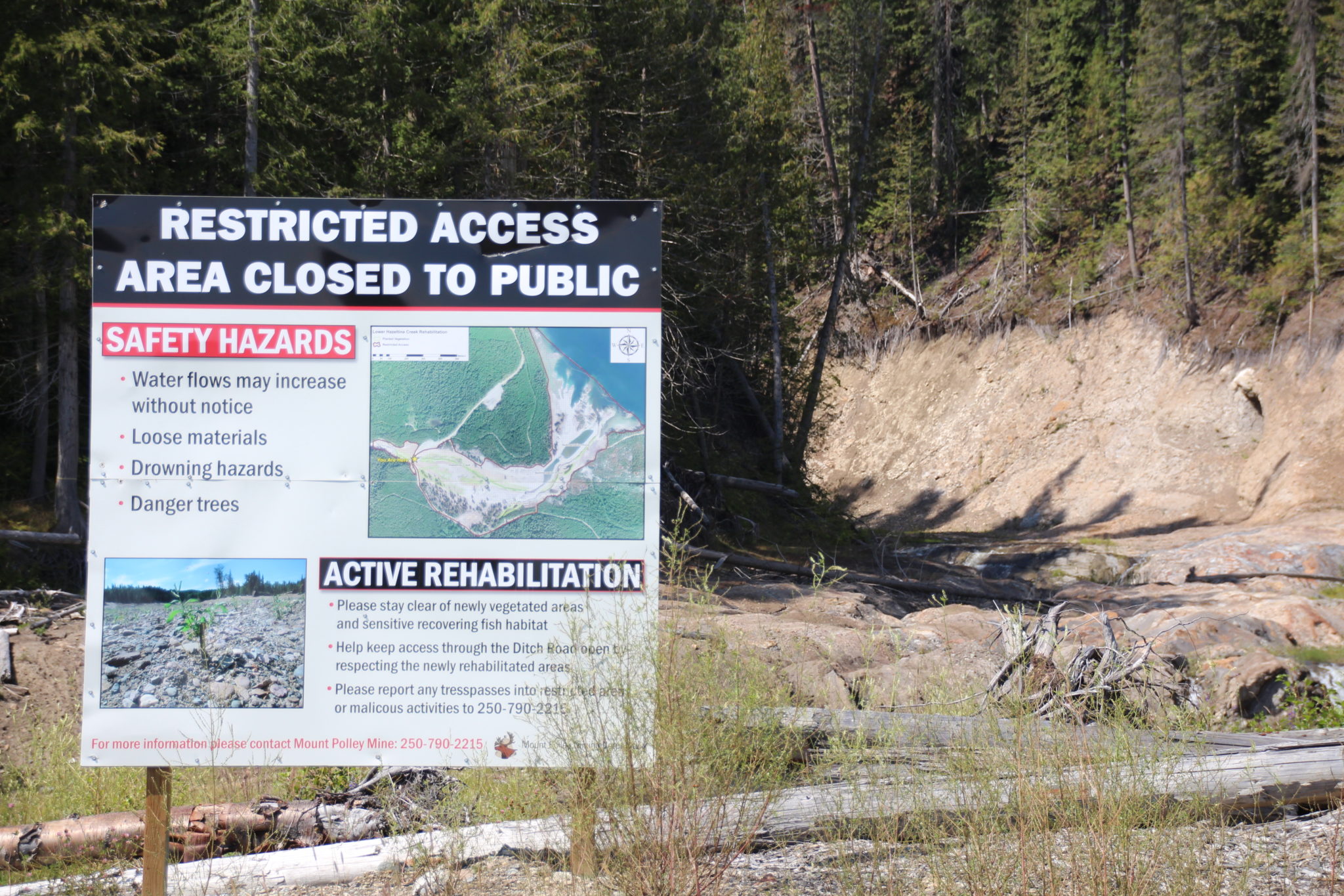 A crater carved out of the earth by the Mount Polley tailings dam burst. A sign is in the left side of the image that reads 'Restricted access, area closed to the public'