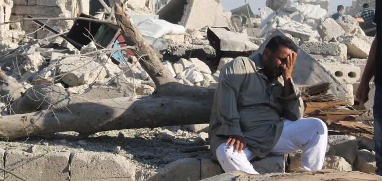 A man sits with head in hands crying on the rubble of his town in Syria