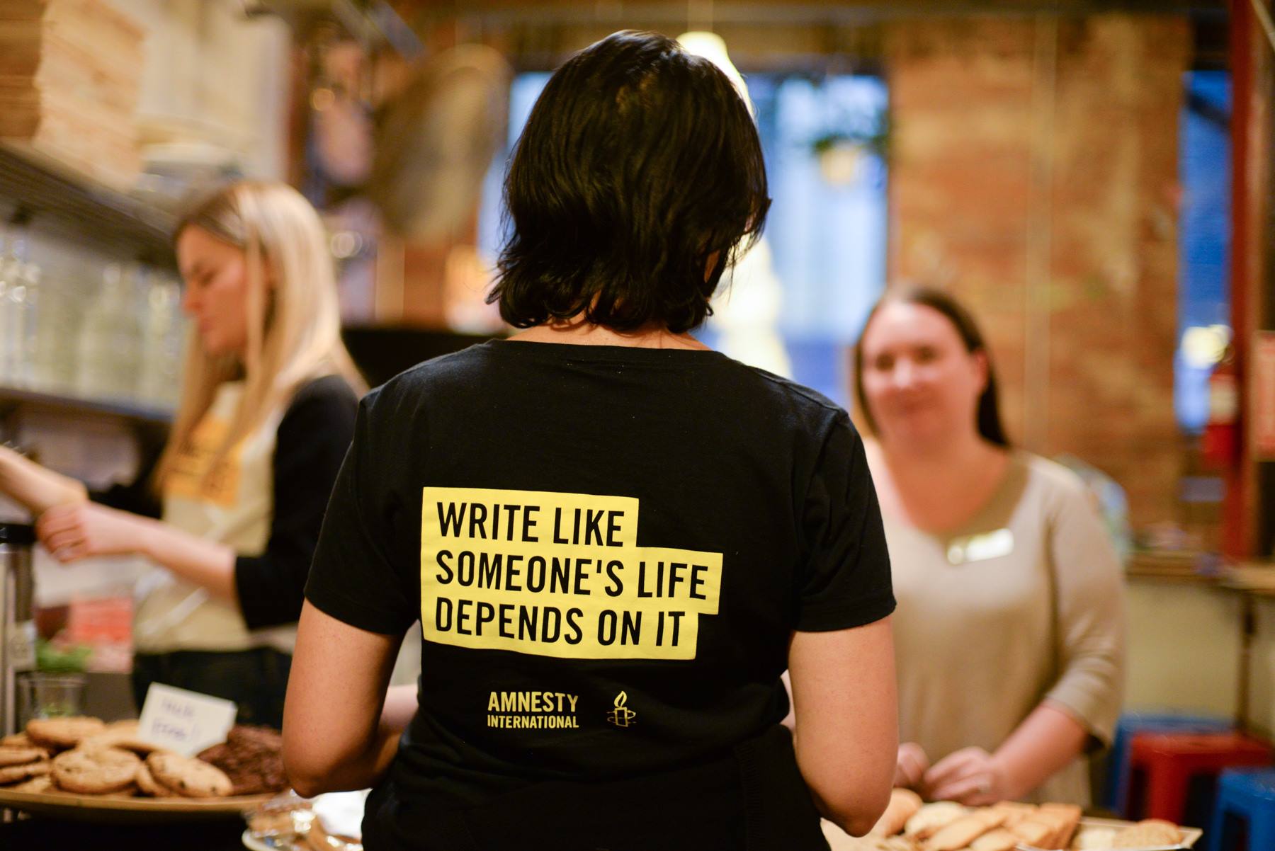The back of an Amnesty supporter with a shirt that reads "Write like someone's life depends on it"