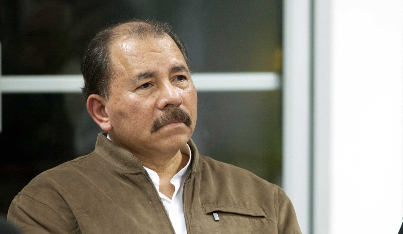 A middled-aged man with a brown mustache wearing a brown jacket over a white, collared shirt.