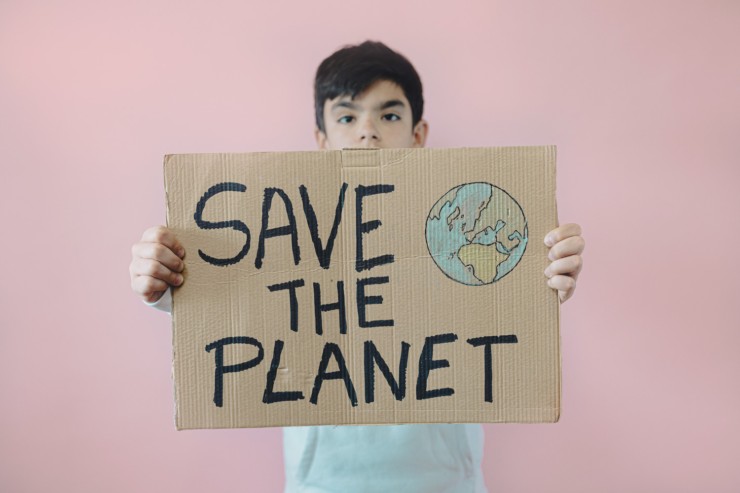 Young teenage boy holding a cardboard sign that says "save the planet."