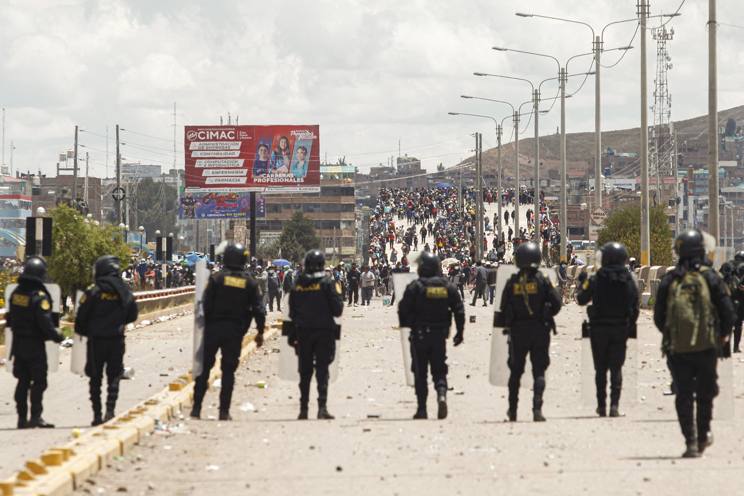 About 10 riot police in full tactical gear stand on a highway facing protesters situated on a hill.