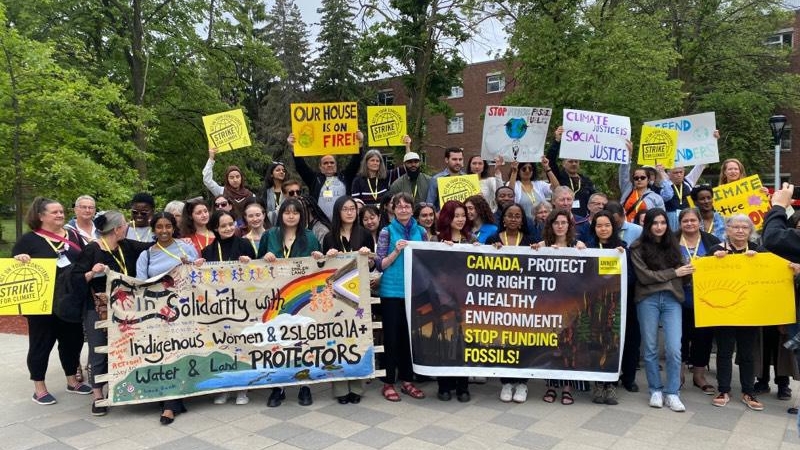 A group of about 40 people holding signs calling on Canada to respect the rights of Indigenous land defenders and to stop funding the extraction of fossil fuels.