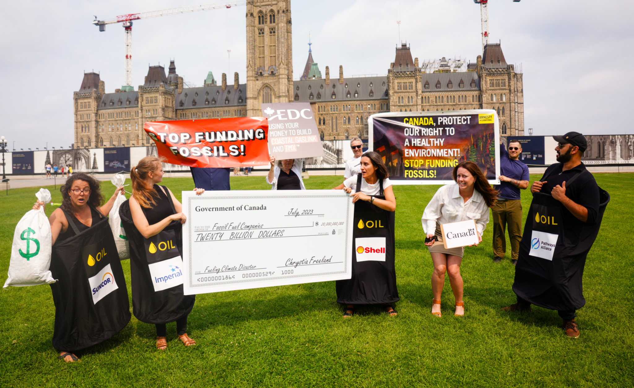 Nine activists on Parliament Hill hold signs calling on the Canadian government to stop funding fossil fuels