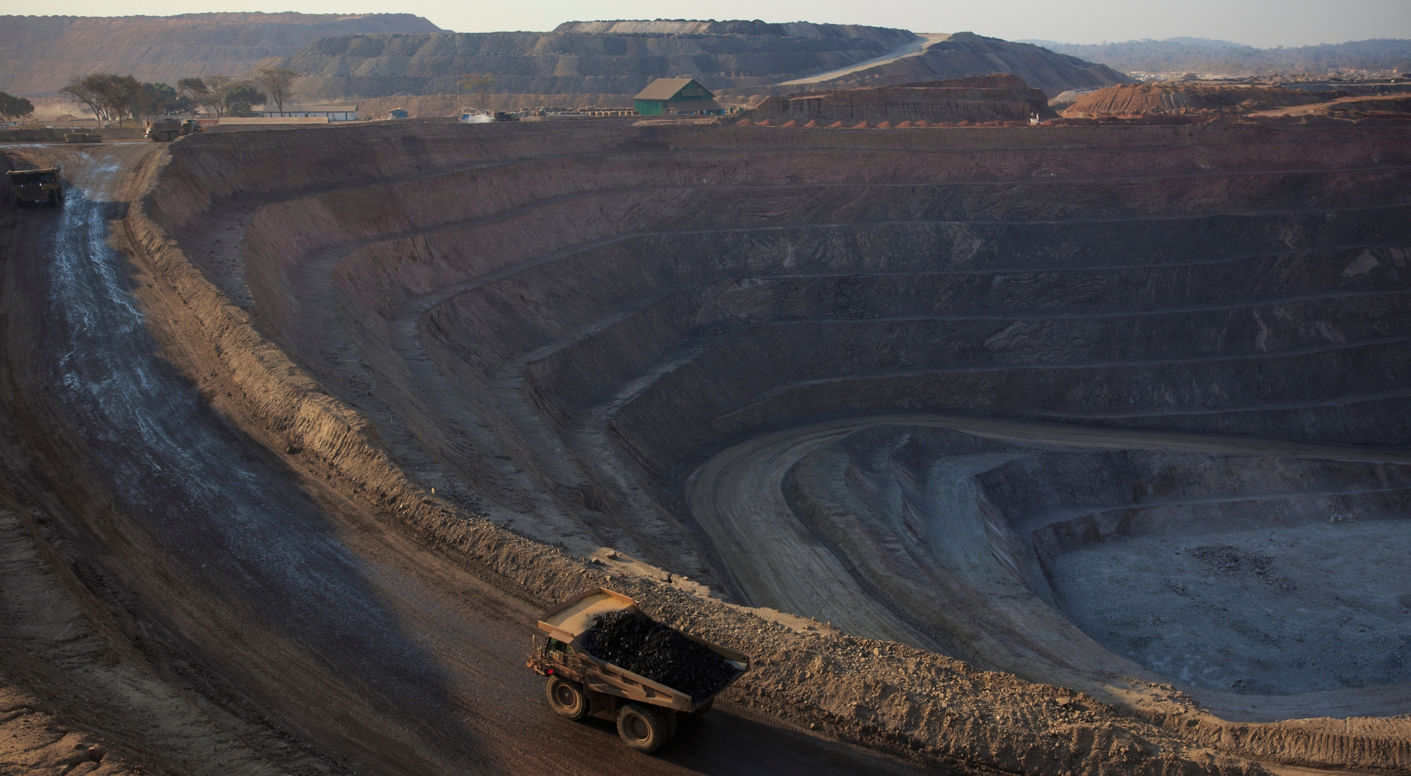 The sun sets on one of the open pit copper mines at Mutanda Mining Sarl on July 6, 2016 in Kolwezi, DRC. The mine is owned (69%) by Glencore, an Anglo-Swiss multinational commodity trading and mining company. The mine is mainly producing copper but also some cobalt. The mine employs about 3,500 people and its located in Luabala Province in Southern DRC. A truck carries a load of ore to the processing plant. (Photo by Per-Anders Pettersson/Getty Images)