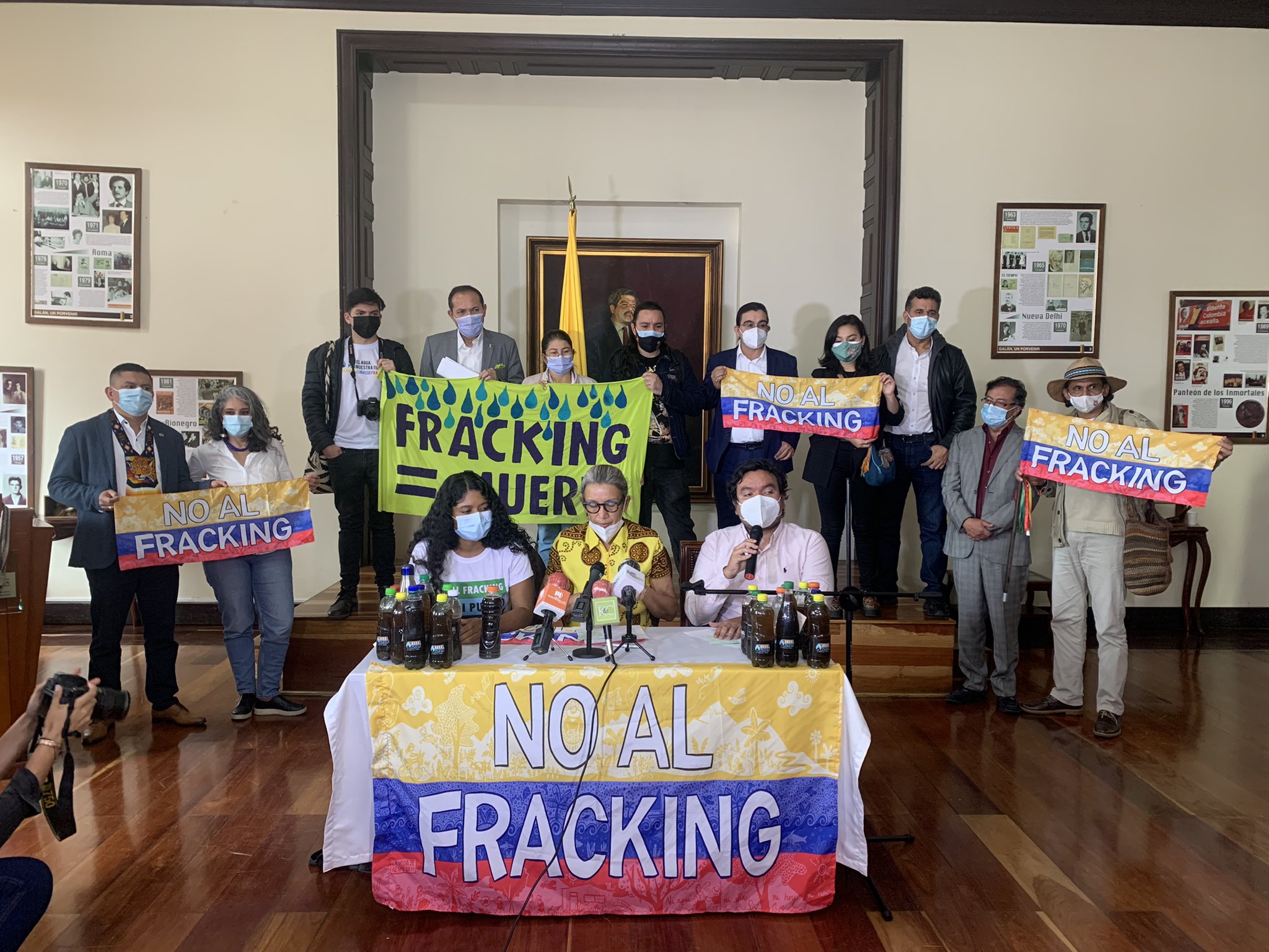 Yuvelis and two other speakers in front of microphones with Banners behind saying NO TO FRACKING and FRACKING EQUALS DEATH