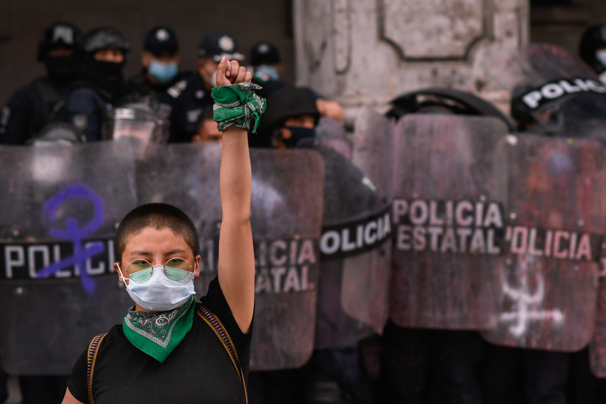 A protestor against gender based violence raises her fist as riot police surround her