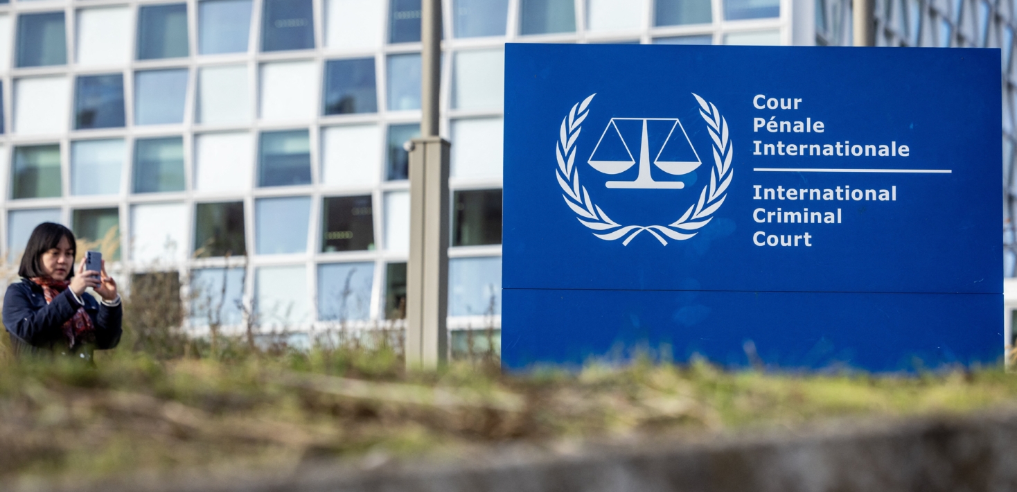 A young women taking a picture of a blue sign that reads "International Criminal Court."
