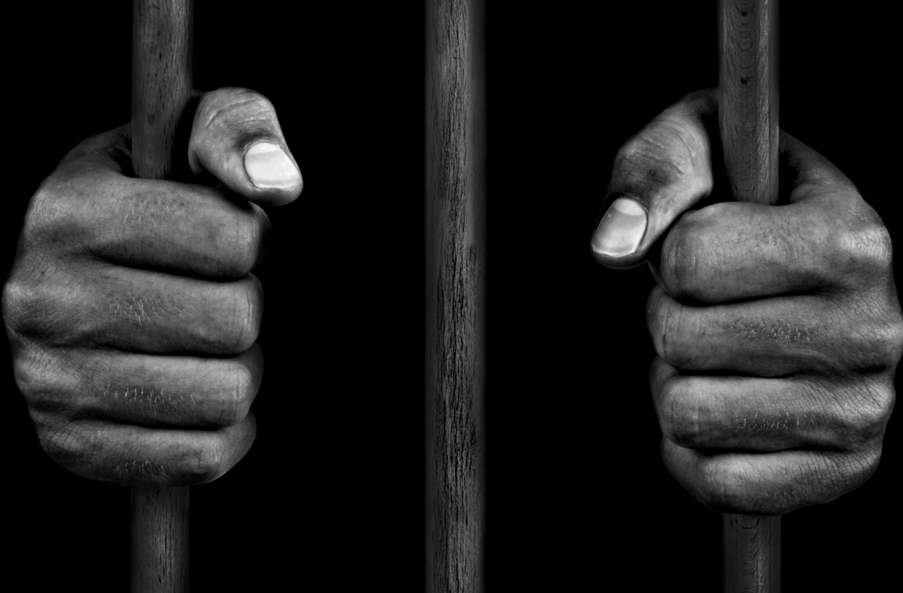 Hands on jail bars in black and white