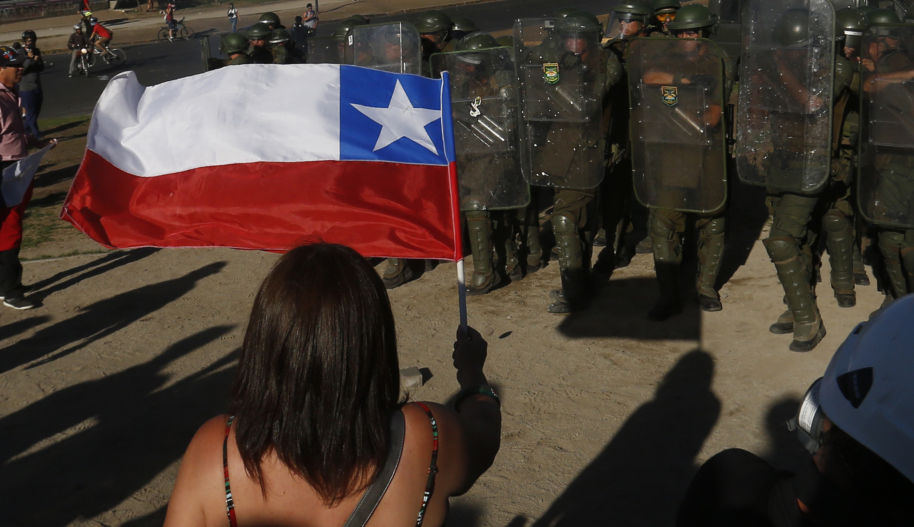 A protestor holds a Chilean flag in front of armed police