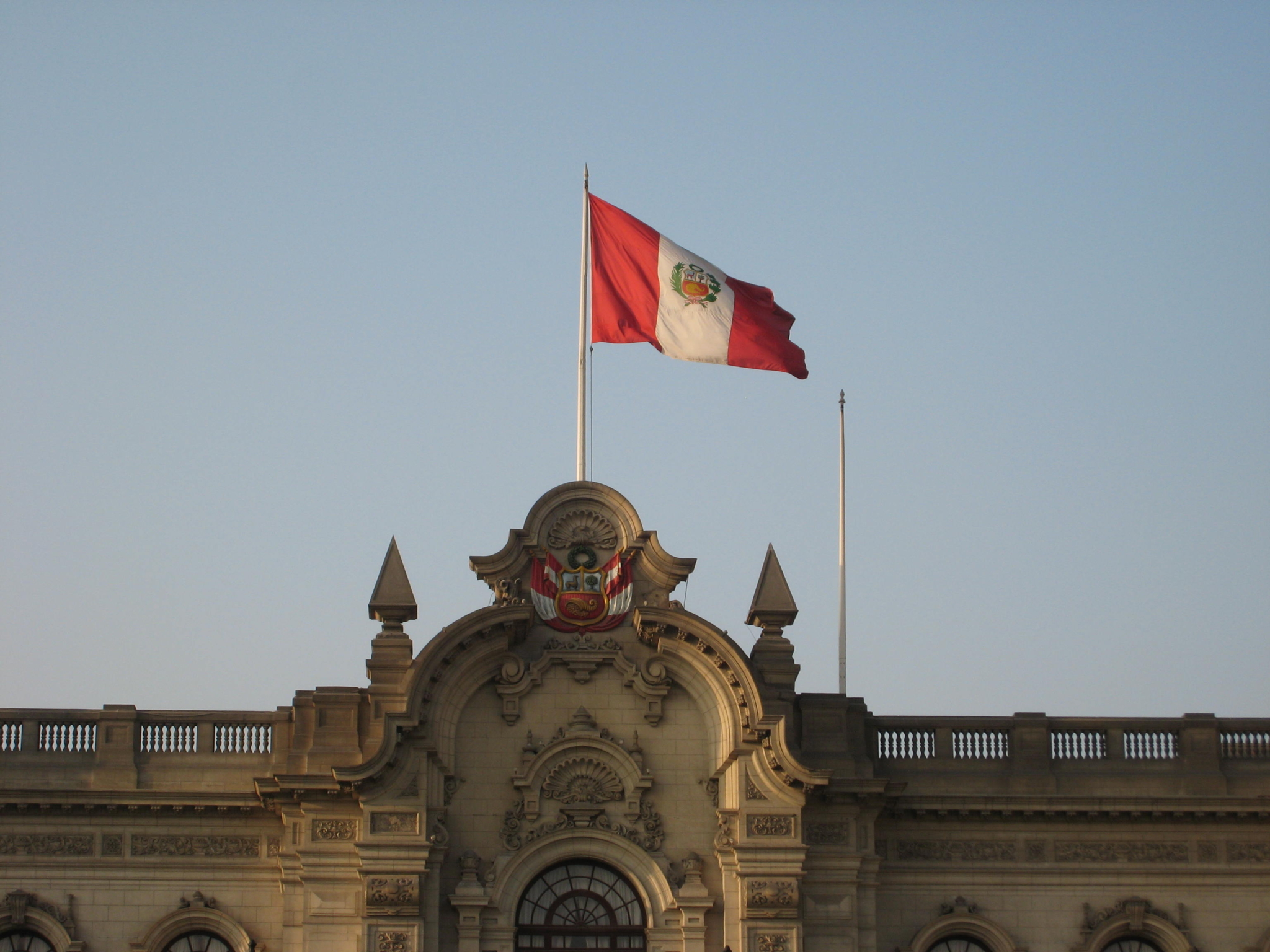 The national flag of Peru waving on a flagpole on top of a Spanish-colonial style building during day time.