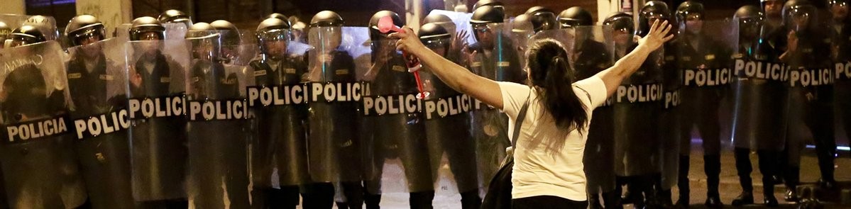 a woman raises out her arms in front of a line of police