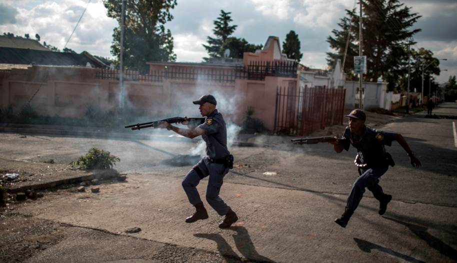 South African police officers fire rubber bullet as they chase protestors in the streets of Johannesburg, on April 23, 2019 during a protest against the lack of service delivery or basic necessities such as access to water and electricity, housing difficulties and lack of public road maintenance.