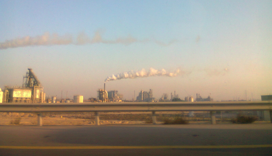In the distance, smoke billows from the smokestacks of an Aramco oil production facility in the desert in Saudi Arabia.