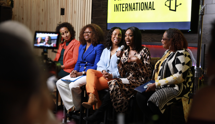 Five women participating in a panel discussion are seated in front of flat-screen TV showing the Amnesty International logo.