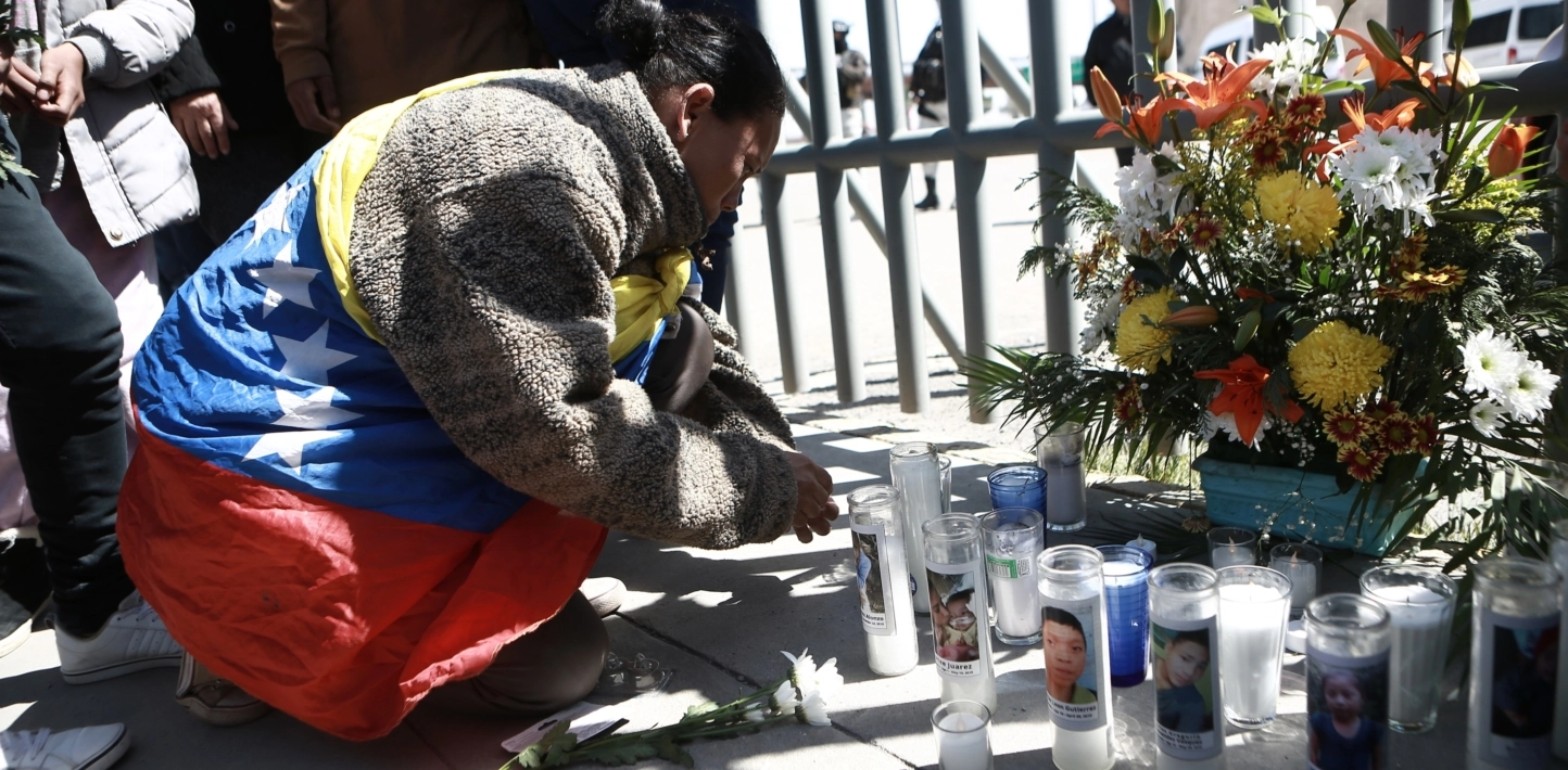 A woman wearing a Venezuelan flag over her fleece sweater kneels down to light a Canada at a vigil outside an immigration detention centre in Mexico where a fatal fire took place.