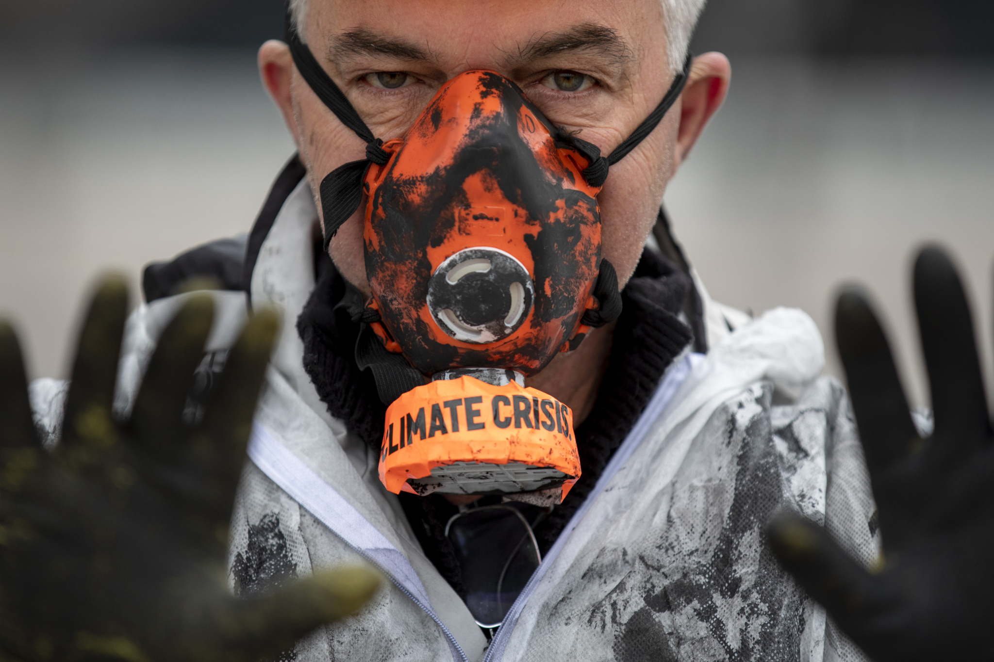 a protestor holds up hands painted black to symbolize contamination by an oil company
