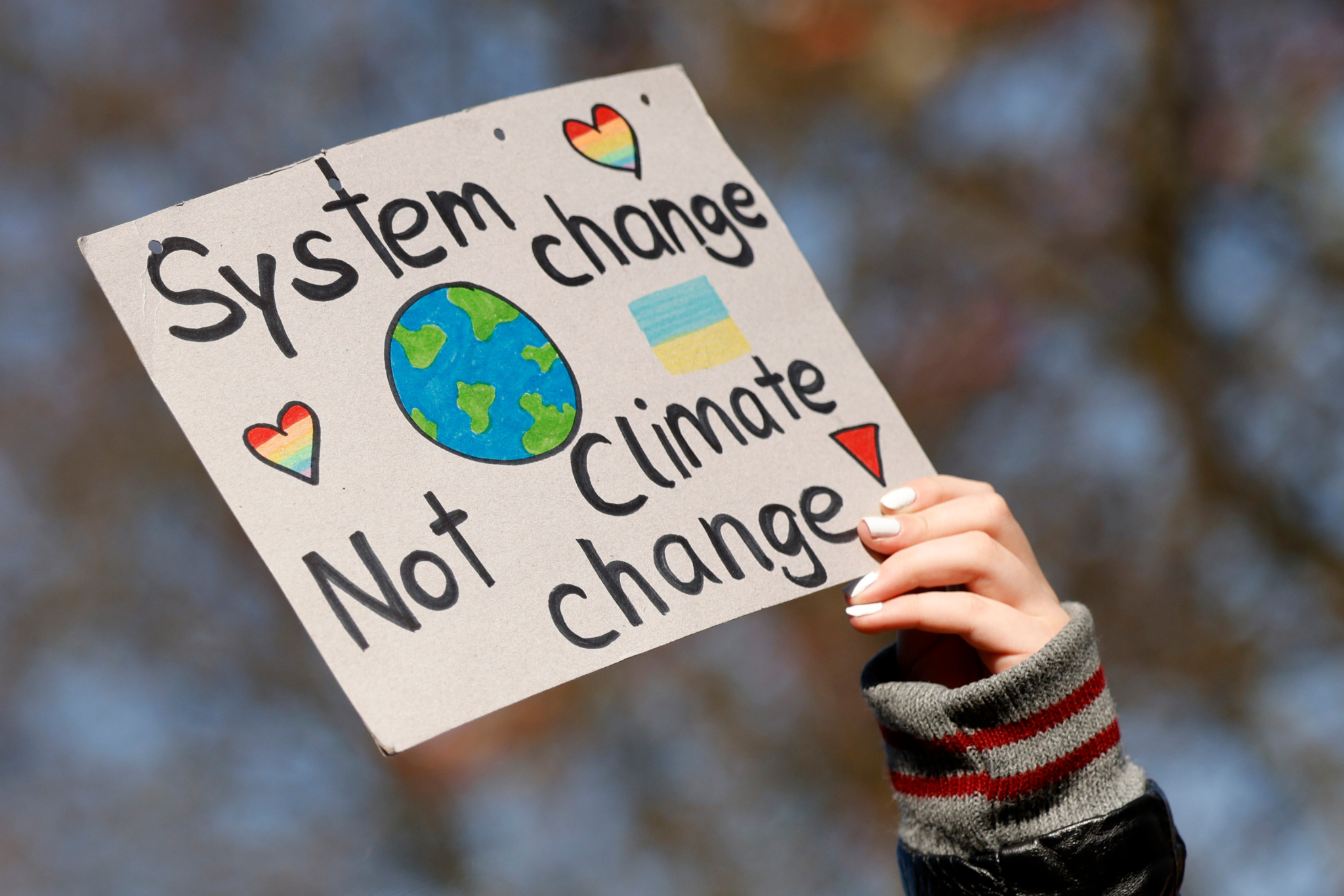 A sign held high has an image of Planet Earth surrounded by hearts and says: "System change. Not climate change"