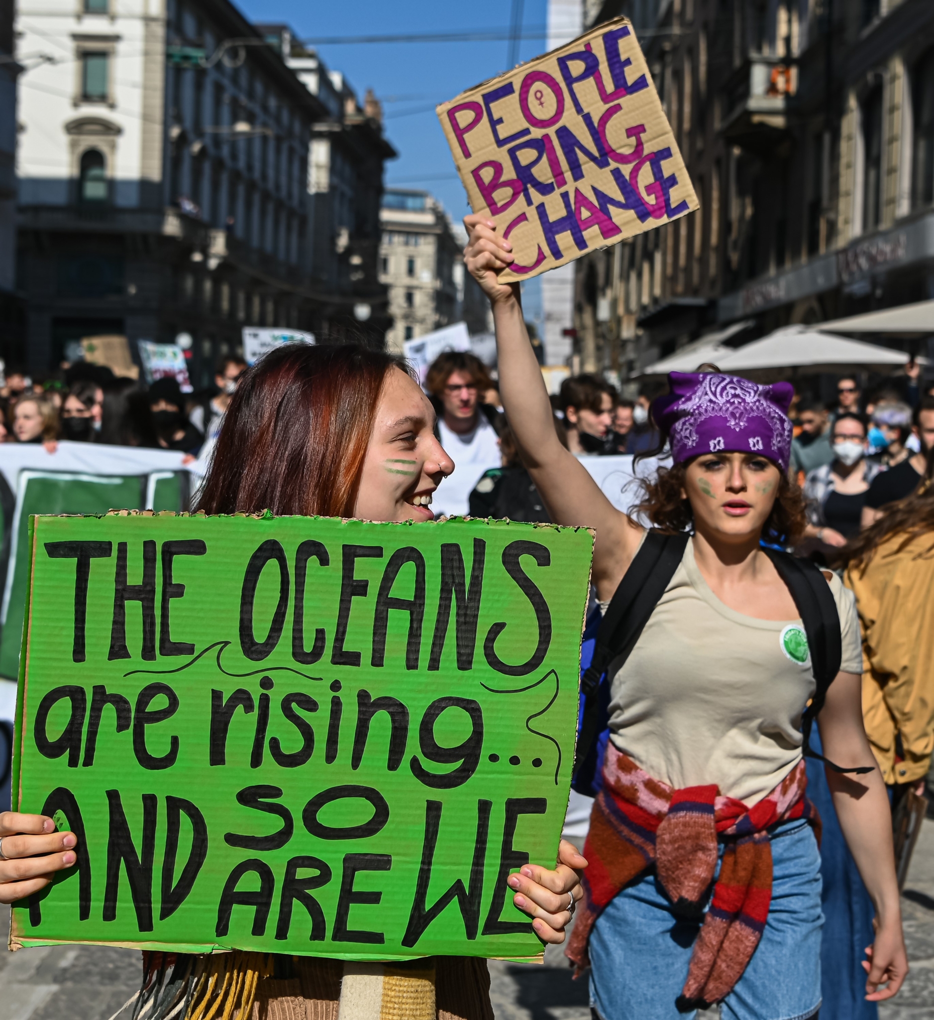 Young women march with signs that say: PEOPLE BRING CHANGE and THE OCEANS ARE RISING, SO ARE WE.