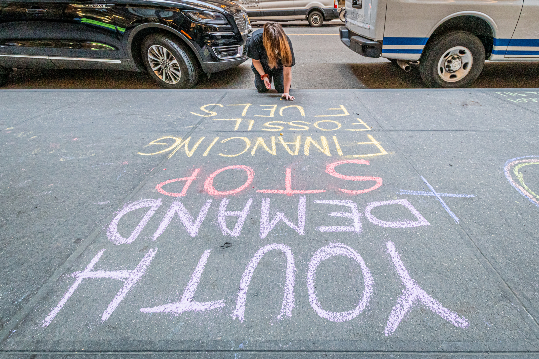 A young person chalks on the sidewalk outside JP Morgan's Annual Shareholder Meeting: Youth demand stop financing fossil fuels 