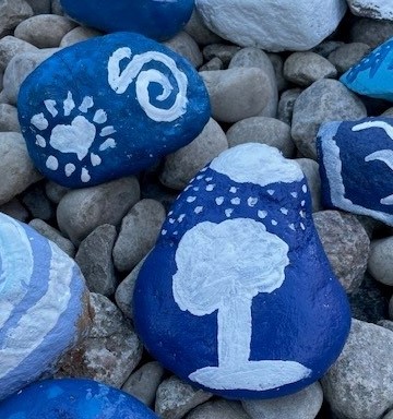 A stone painted with a tree, sun and rain. 