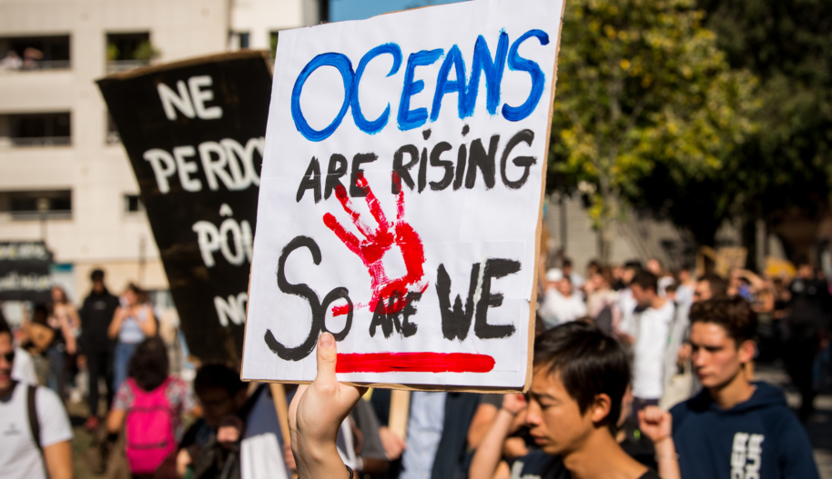 A hand raising up a protest sign that reads "Oceans are rising, so are we."