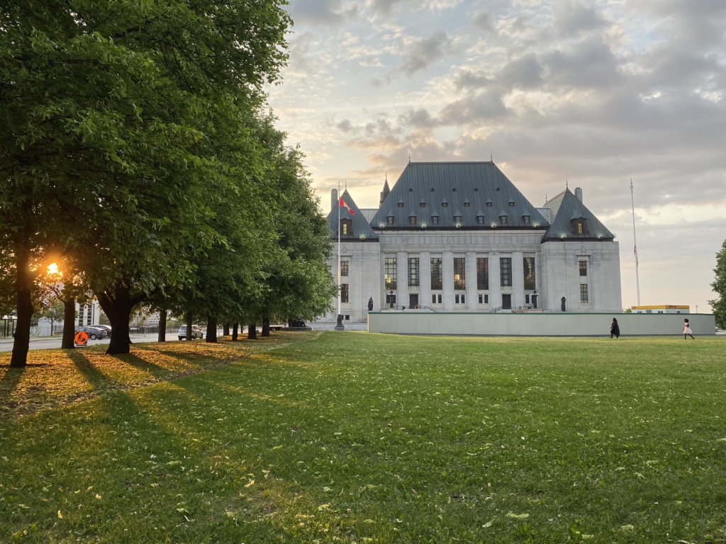A granite neoclassical building with steep green rooves with a partially cloudy sky at sunset.