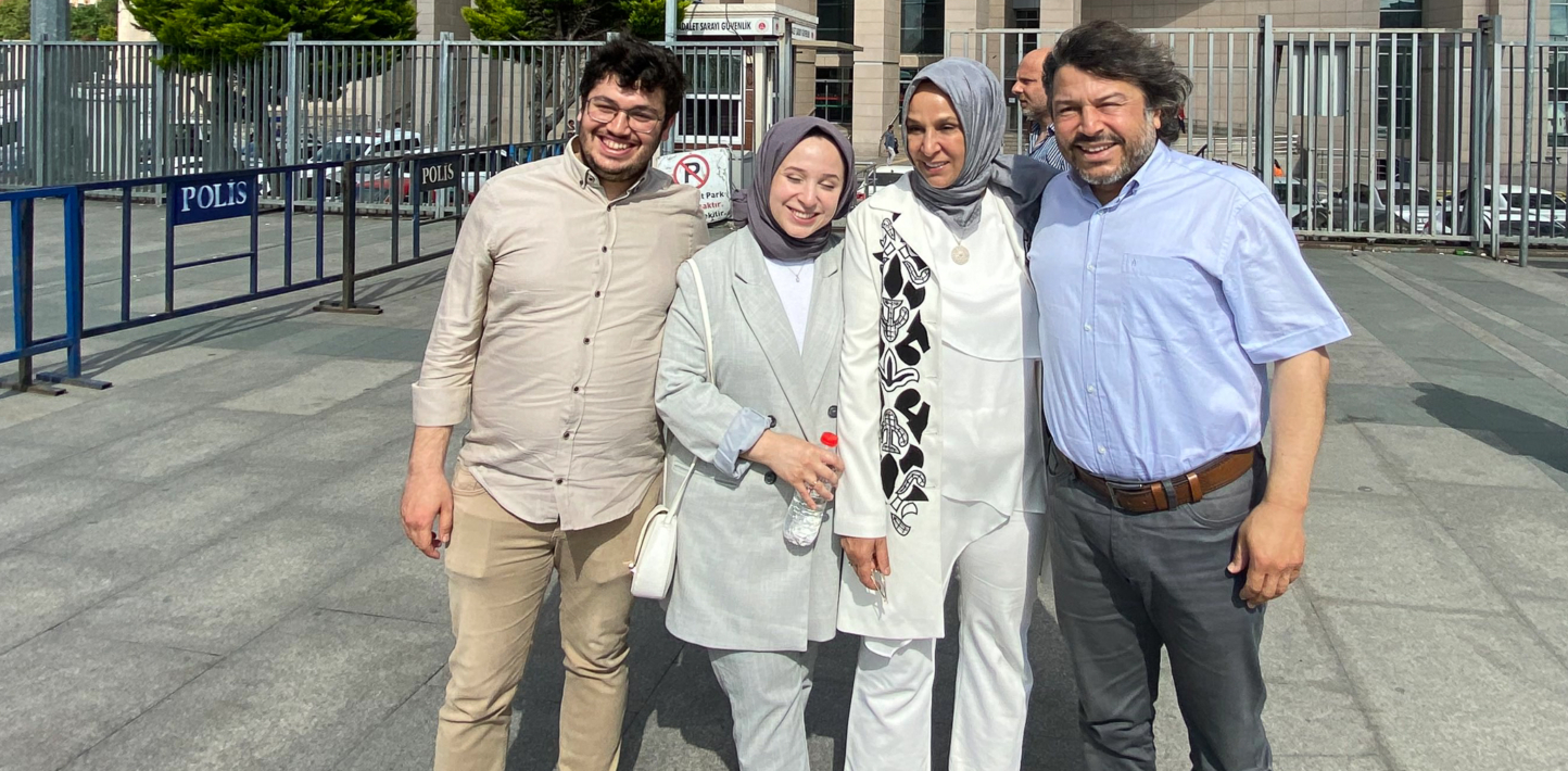Four people — two men on the outside and two Hijab-wearing women on the inside — smile for the camera outside a police station.