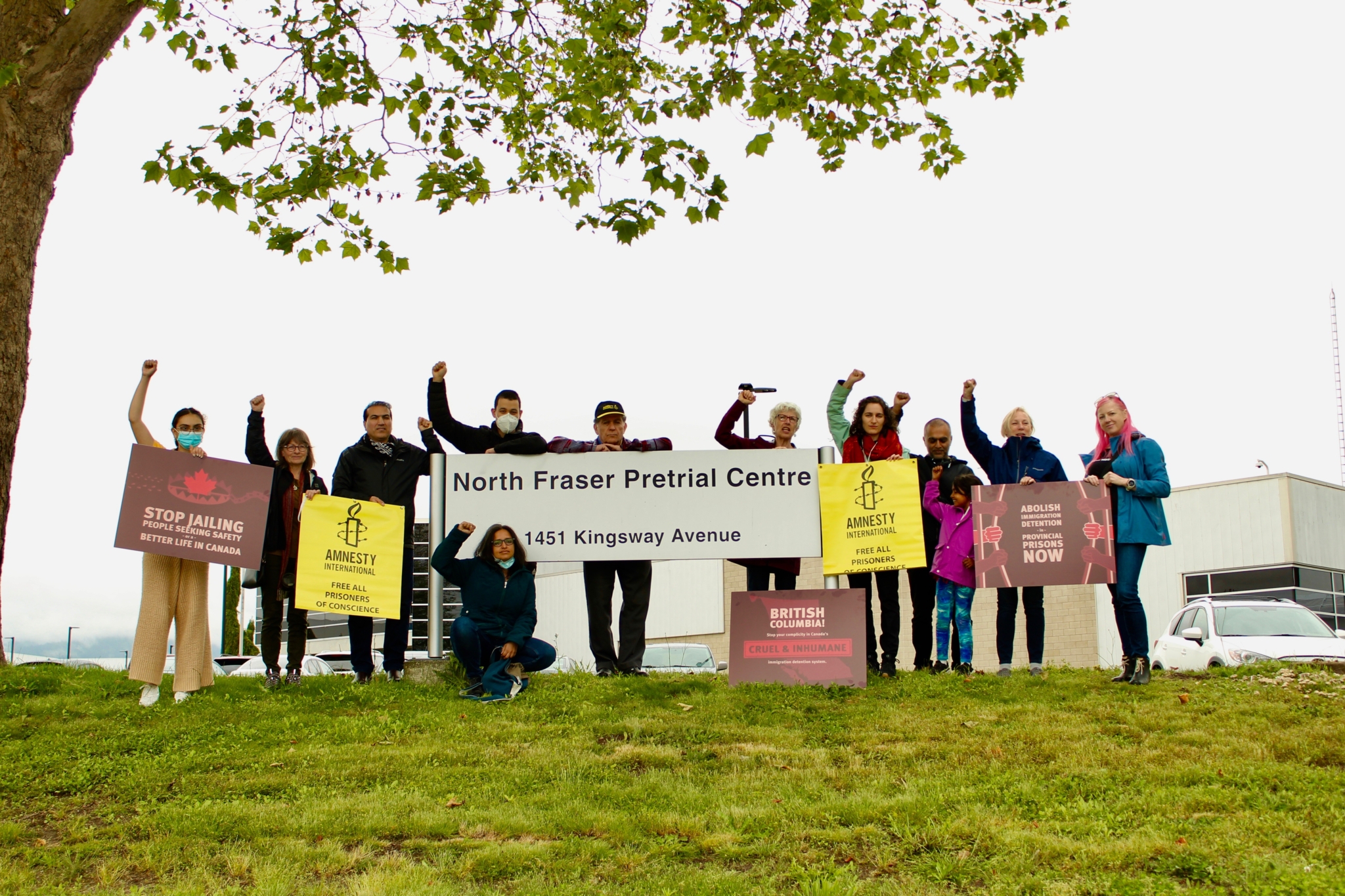 About a dozen people raise their fists an hold signs outside a prison at a rally opposing immigration detention in British Columbia's provincial jails.