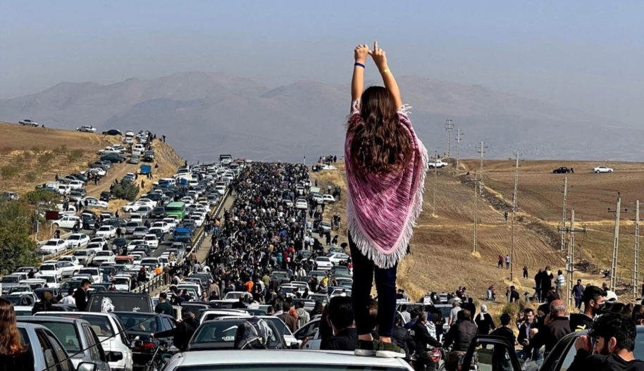 This 26 October, 2022, dated image posted on Twitter shows an unveiled woman standing on top of a vehicle as thousands make their way toward Aichi cemetery in Saqez, Mahsa Amini's hometown in the western Iranian province of Kurdistan, to mark 40 days since her death. © Private