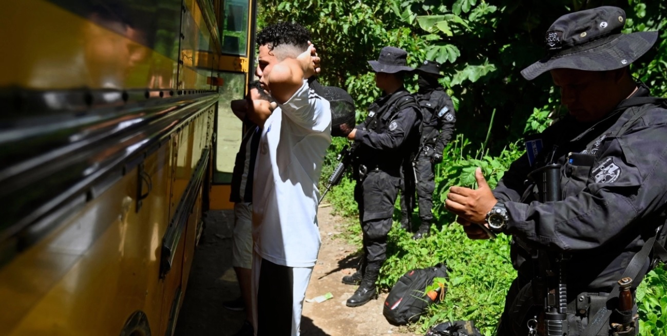Masked, heavily armed police remove young men from a bus and keep them with their hands behind their heads.