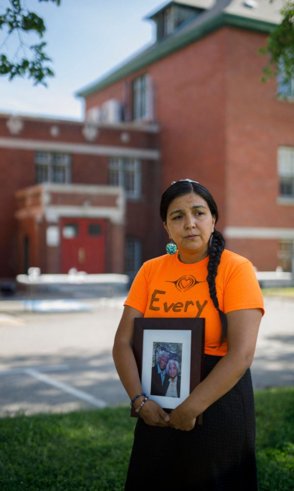 Stephanie Gutierrez holds a photo of her grandmother Tillie Gutierrez, a survivor of the Kamloops Indian Residential School, and grandfather Allan Gutierrez, in front of the school on June 2, 2021. (Photo by Cole BURSTON / AFP via Getty Images)