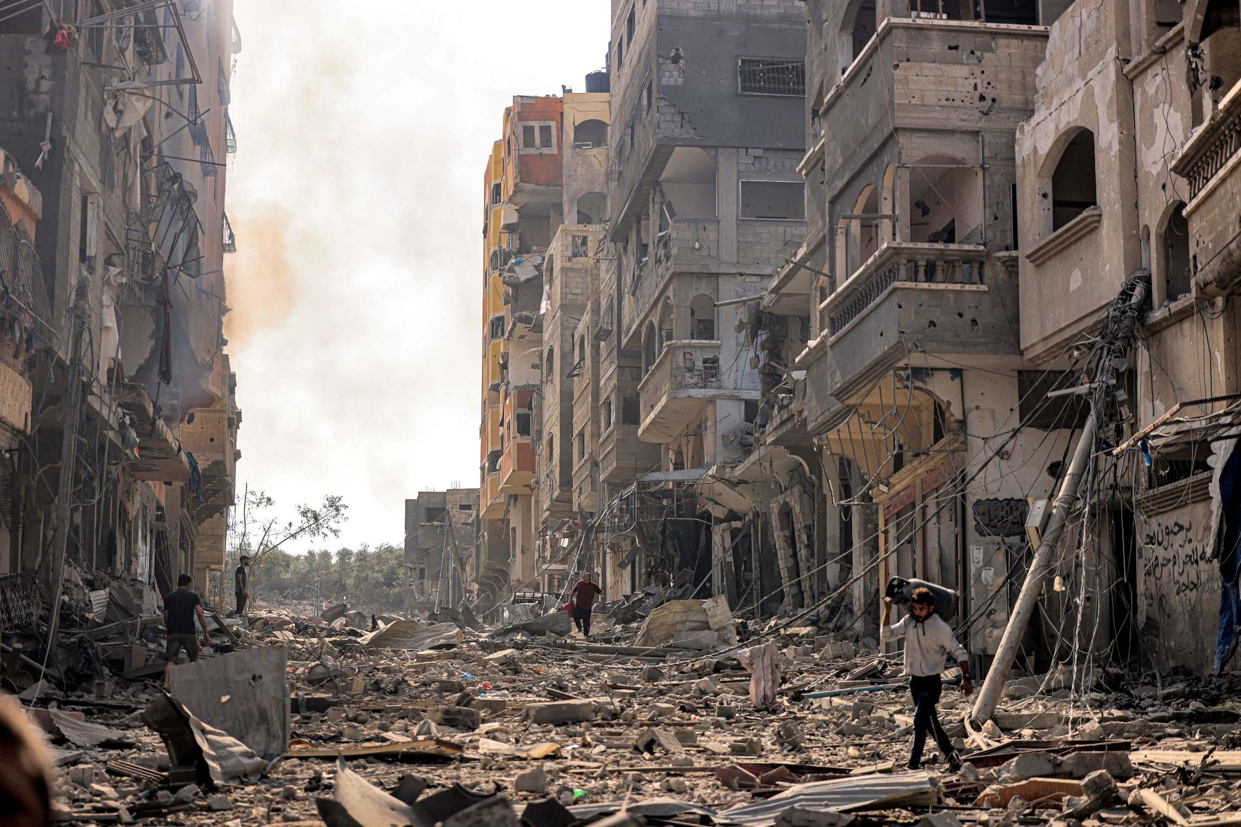 Civilians in Gaza at unprecedented risk as Israel imposes communication black-out during bombardment and expanding ground attacks. A man carries a propane gas cylinder on his back while walking through debris and destruction littering a street in the Jabalia camp for Palestinian refugees in Gaza City on October 11, 2023. Photo by MAHMUD HAMS/AFP via Getty Images.