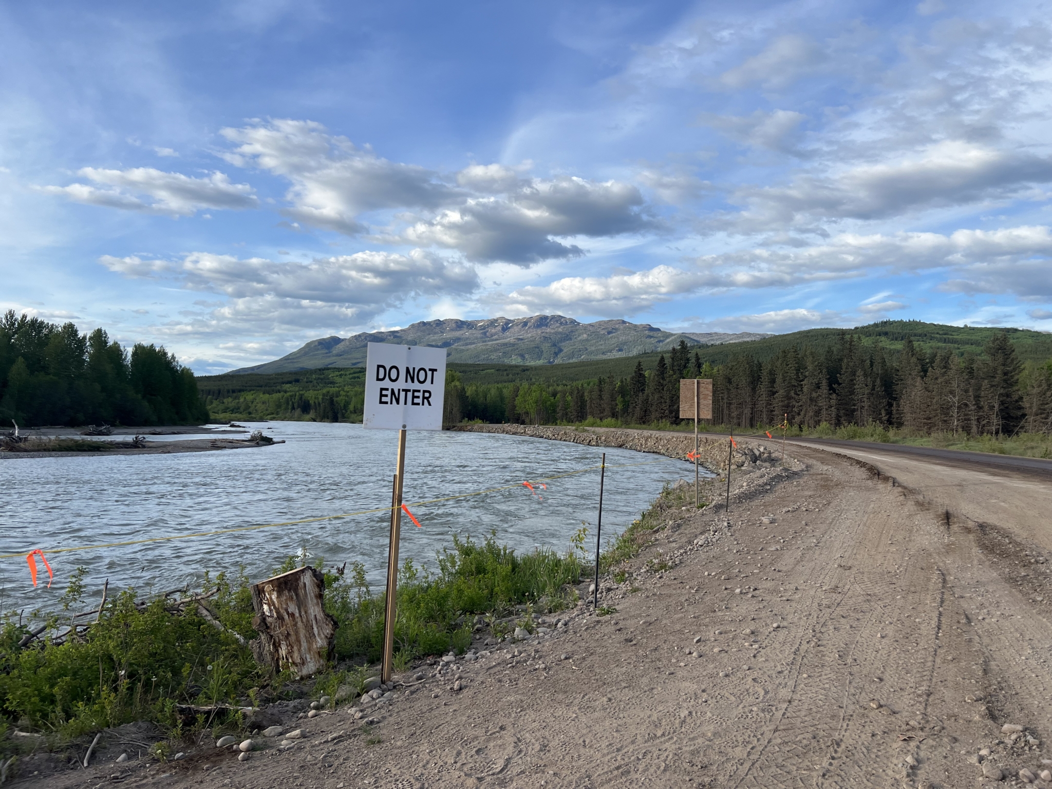 A sign that reads "Do Not Enter" located on the side of a dirt road near a riverbank.