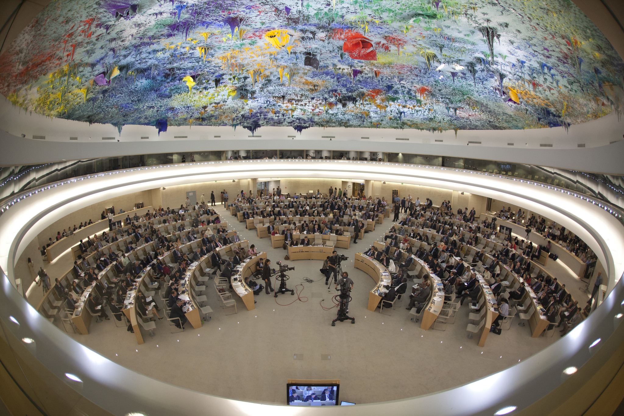 A circular room with a brightly coloured mural on the ceiling and eight concentric semi-circles of seats on the floor.