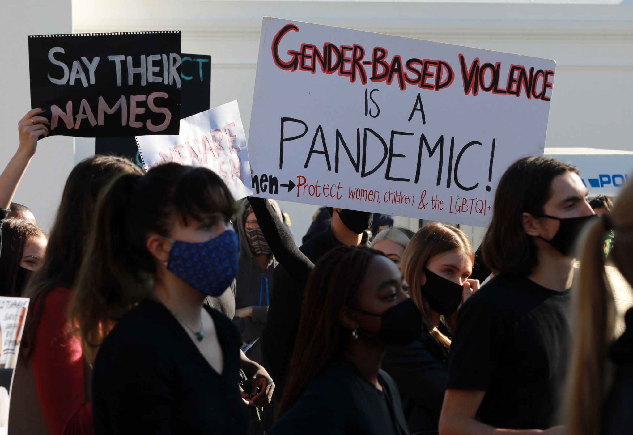 Women protest holding signs that read "Gender-Based Violence is a Pandemic" and "Say Their Names"