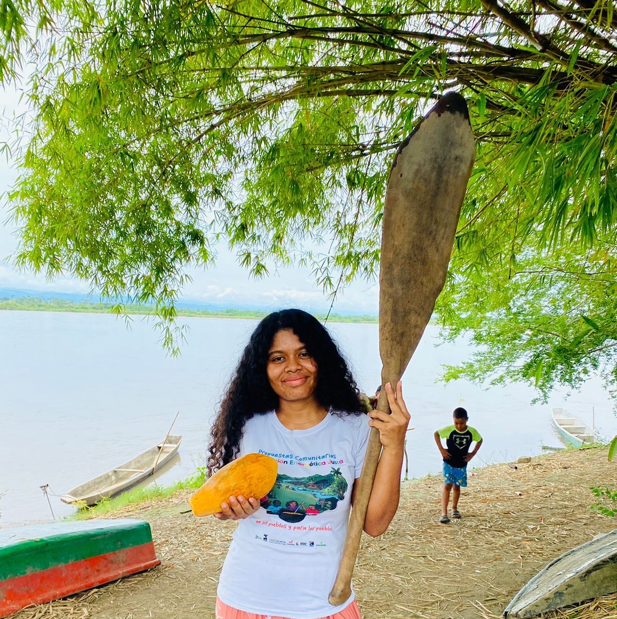 Yuvelis Morales beside the river holding a paddle and a papaya