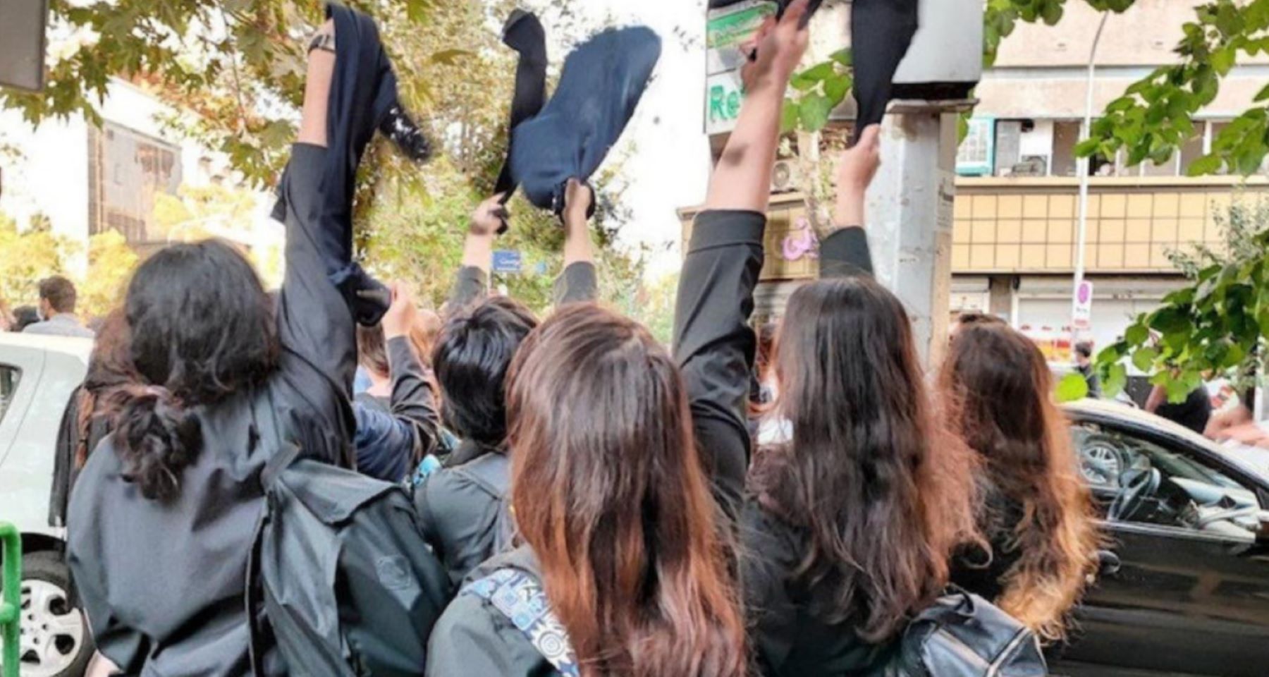 Iranian female students pictured from the back with their hair uncovered and raising their compulsory veils in the air. © private