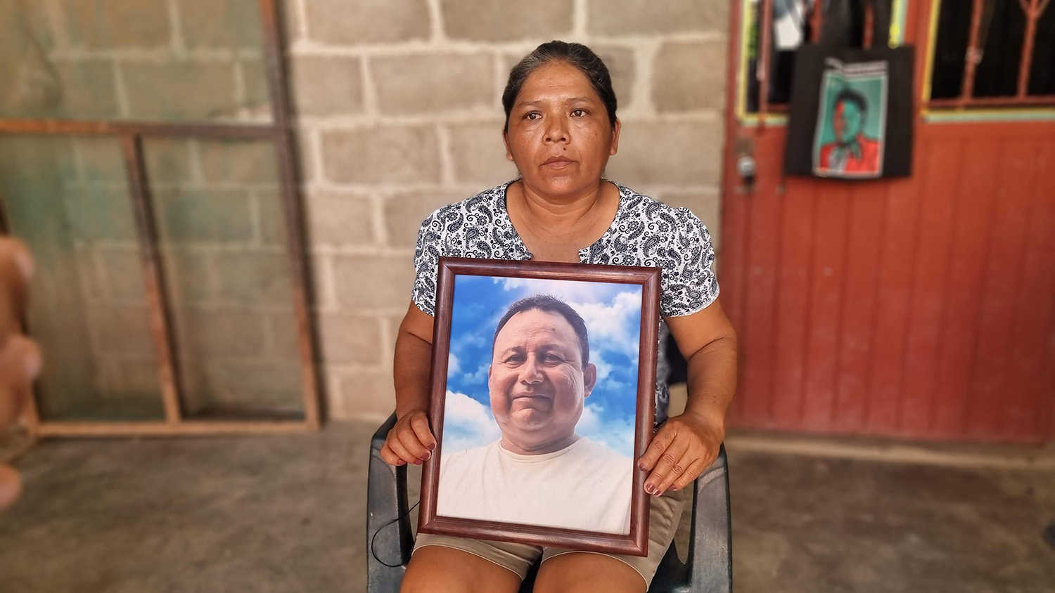 A woman sitting in a chair holds a portrait of her late husband, a Mexican journalist who was assassinated for his reporting.