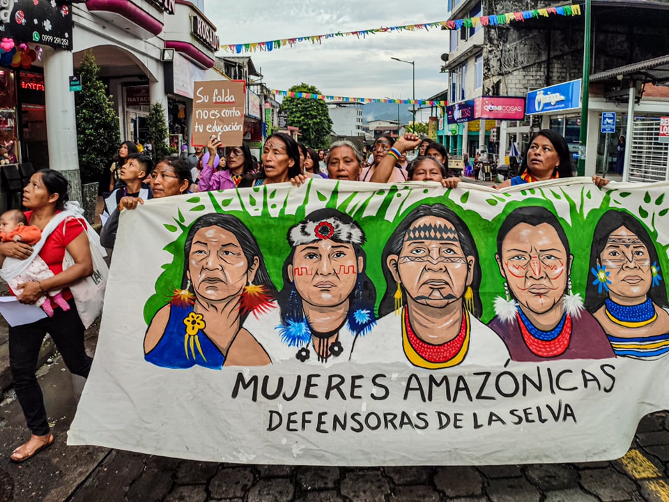 Amazonian women take part in a march holding a huge banner
