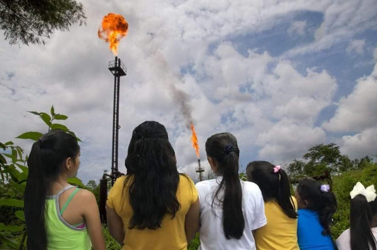 Six young girls with their backs to the camera. They're looking at a gas flare