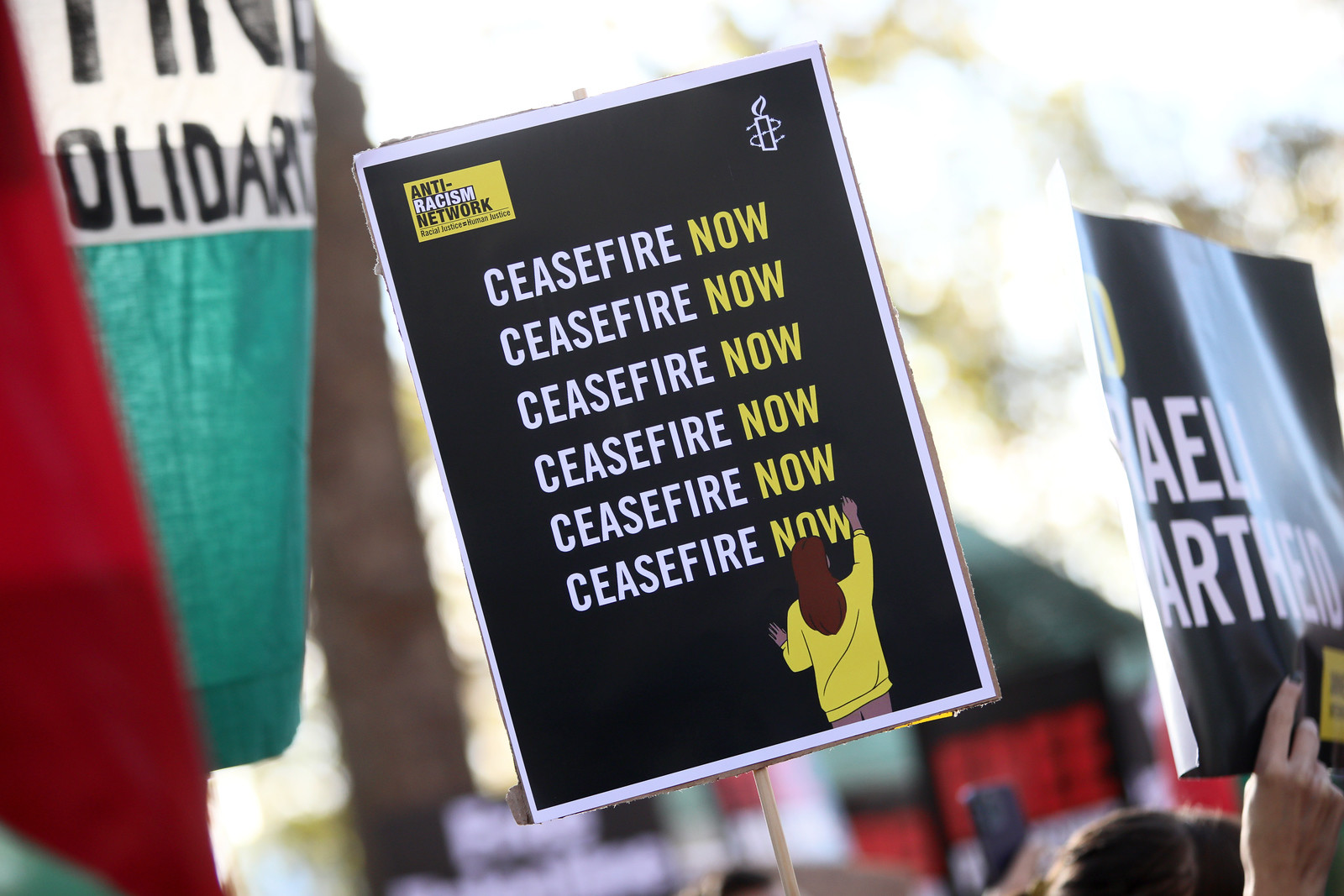 A black sign with the text "Ceasefire Now" written on it six times.