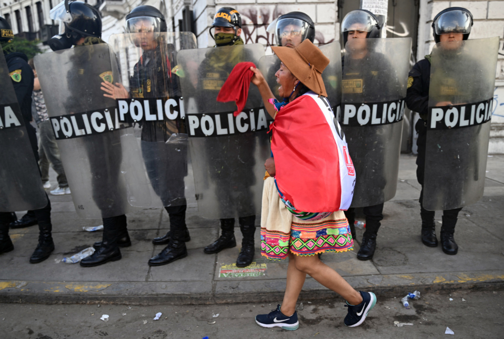 An Indigenous woman walks in front of riot police during a protest demanding the resignation of Peru's President Dina Boluarte in Lima on January 23, 2023.