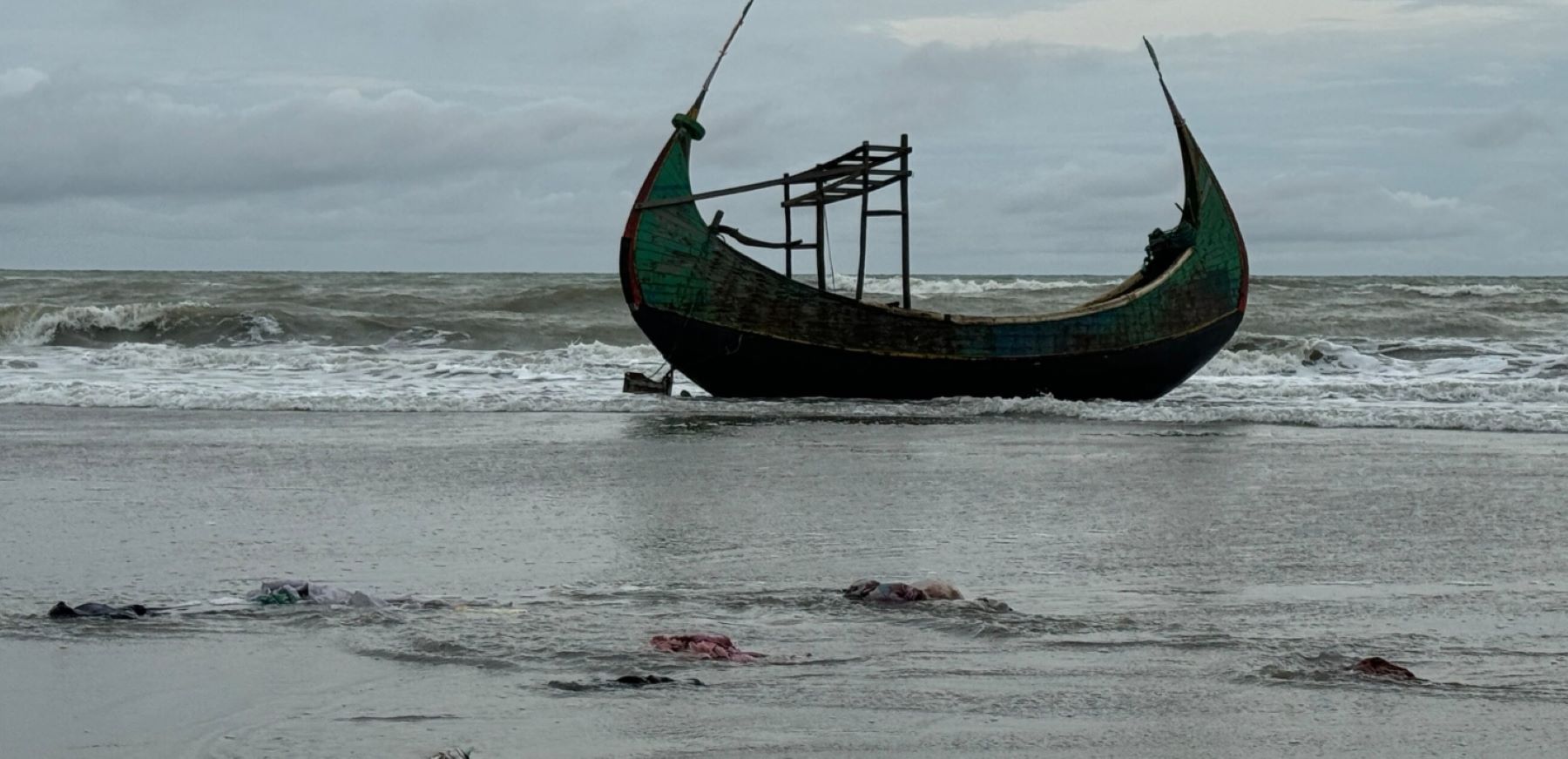 In the early morning of August 6, 2024, about 250 Rohingya survivors fled bomb attacks in Myanmar, crossing into Bangladesh in several boats via the Naf River. They arrived at Marine Drive near Teknaf in Bangladesh, where one of the boats capsized, resulting in the deaths of several Rohingya men, women, and children. This photo from August 6, 2024 shows one of the boats that carried the survivors. The foreground is strewn with clothes and sandals belonging to Rohingya who fled. © Shafiqur Rahman