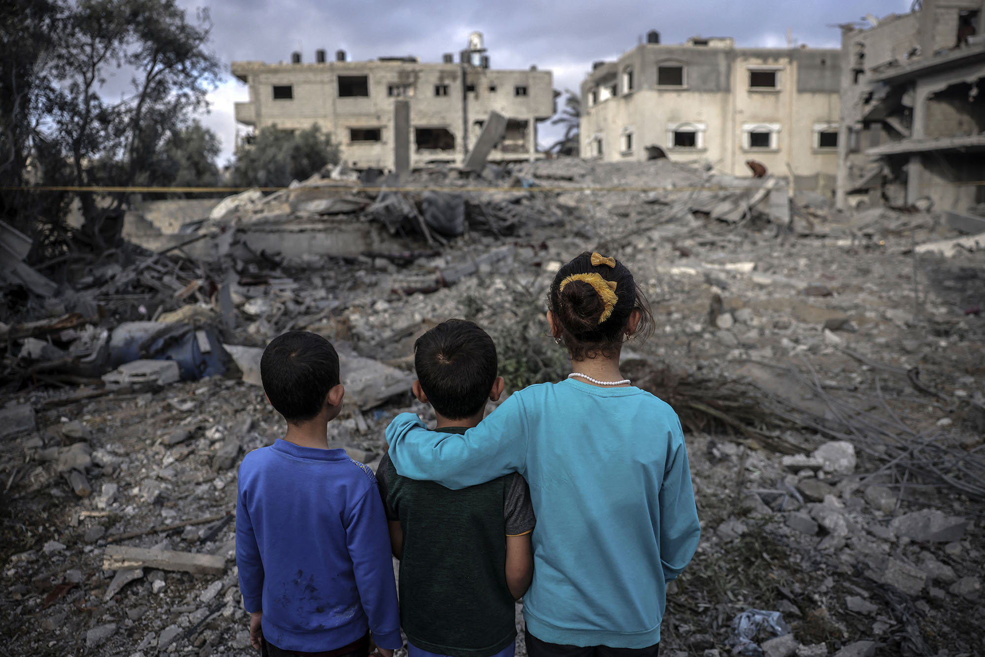 3 Palestinian children looking out at the destruction and rubble of their homes in Gaza