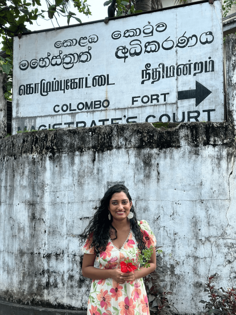 Woman smiling in front of a concrete wall with a sign on it, holding flowers